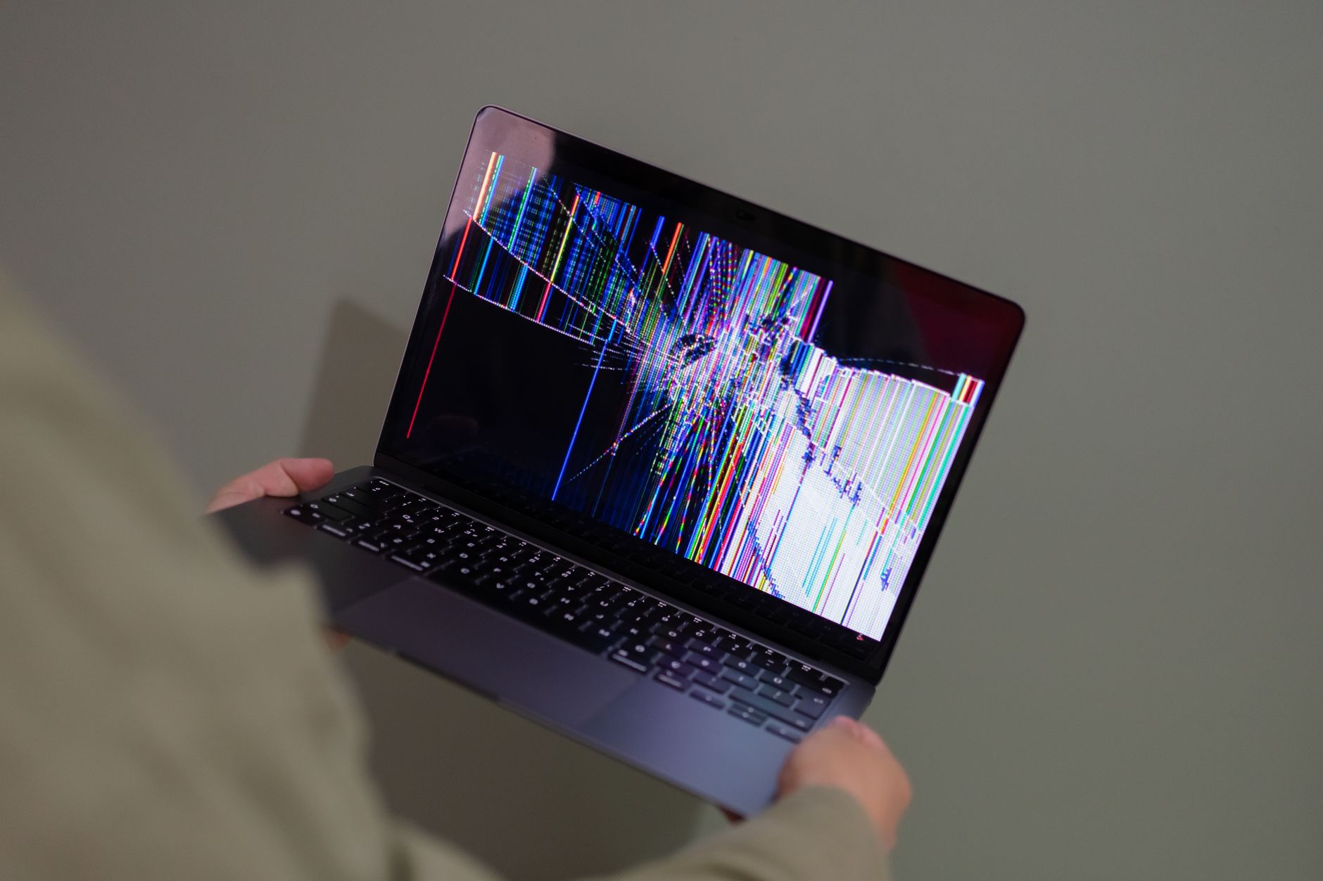 Osoba trzyma laptop z pękniętym ekranem i kolorowymi zakłóceniami