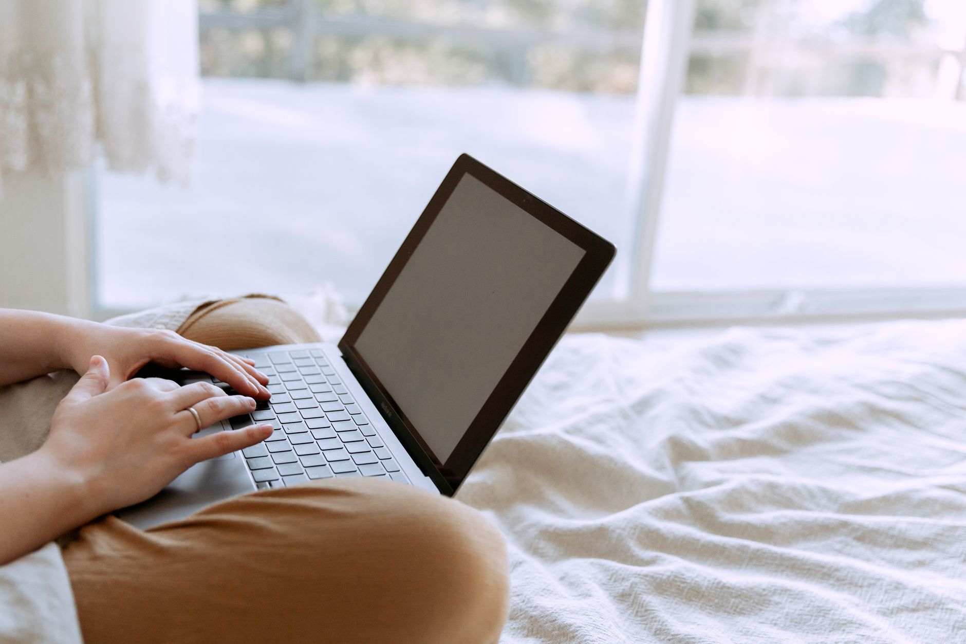 Osoba z netbookiem medytuje na łóżku przy oknie w domu